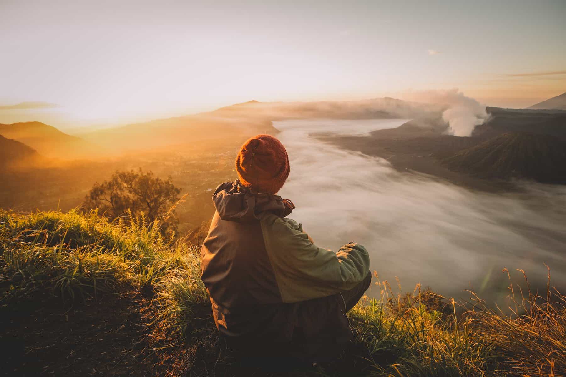 man sitting on the hill and looking at landscape at dawn