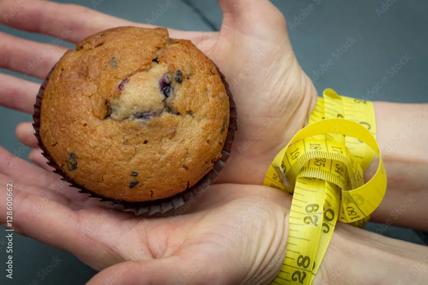 Diet, bondage and delayed gratification concept with woman hand reaching for a muffin while her hands are tied together with measuring tape a symbol of dieting and self control.