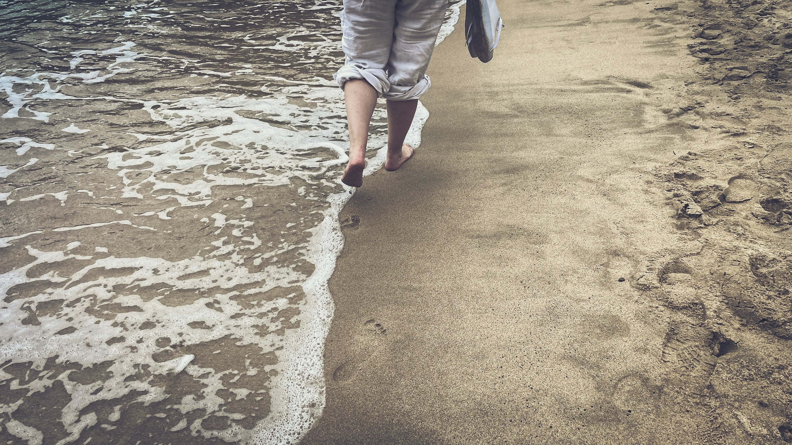 A man walking along a beach next to the ocean stockpack unsplash